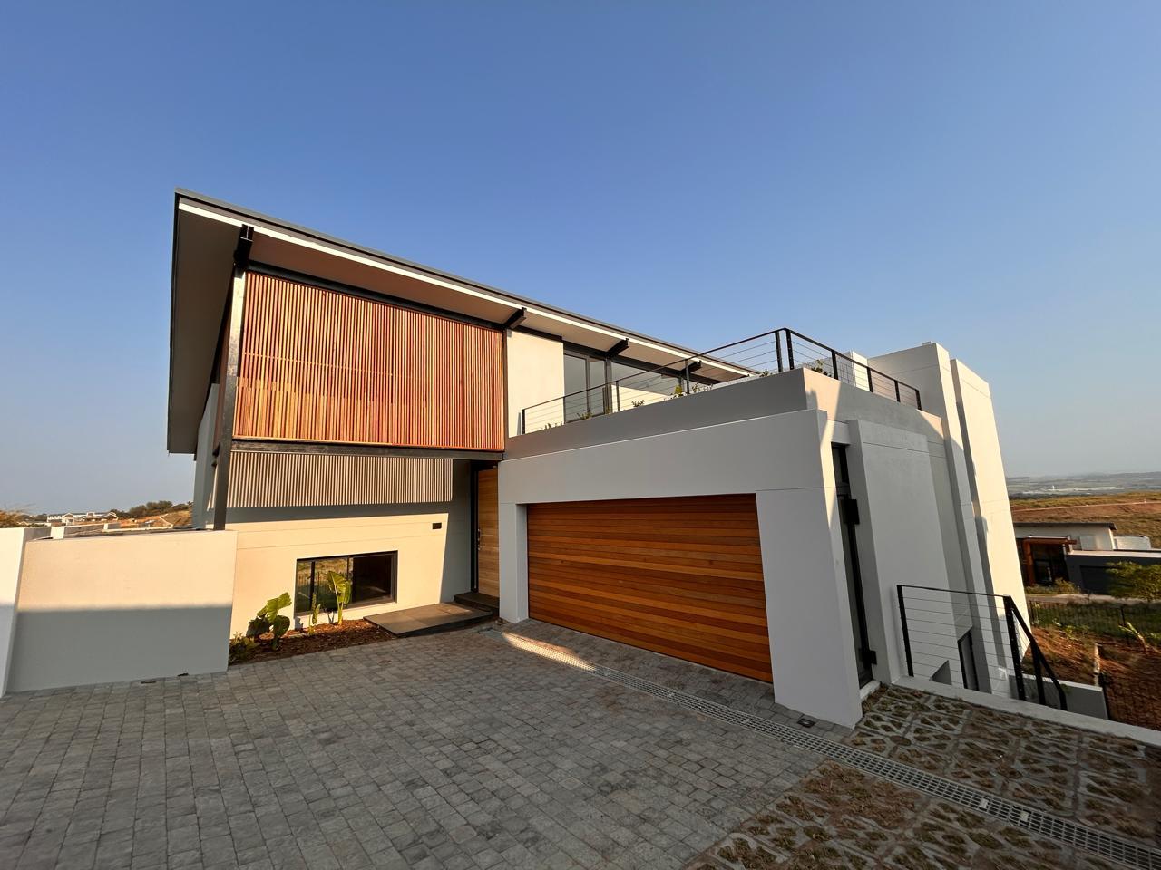 Front elevation of a new home with a timber slat screen, roof terrace, cedar garage door and paved driveway