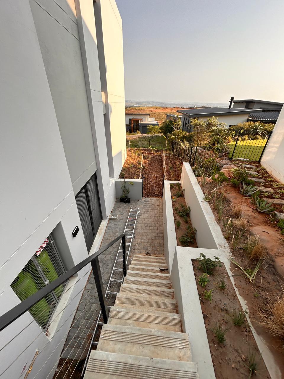 Outdoor concrete stairway with a steel cable balustrade descending past planted retaining walls