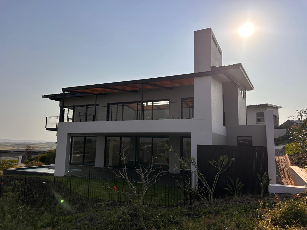 Rear view of a double-storey home at sunset with a pool, lawn, covered terrace and wraparound balcony