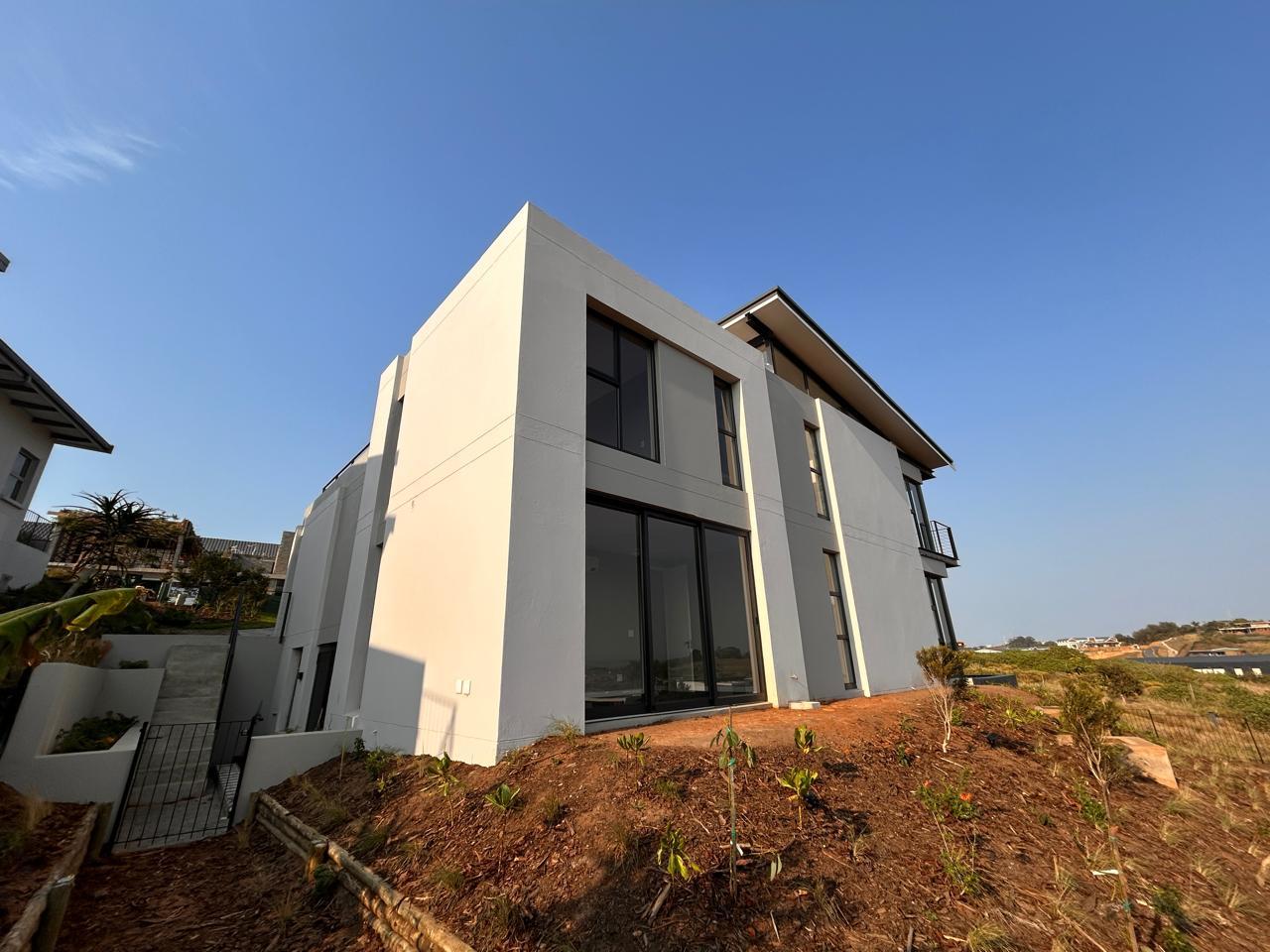 Side elevation of a white double-storey home with tall black-framed sliding doors and a newly planted garden