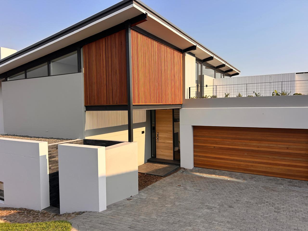 Completed home entrance with a timber slat screen, timber front door, cedar garage door and paved driveway